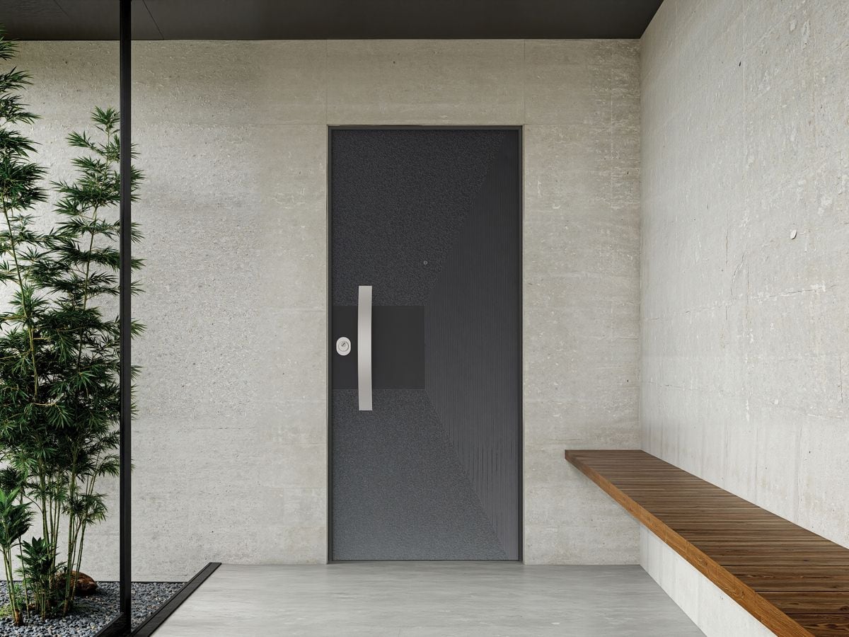 Porte blindée anthracite à motif géométrique, sous un porche en béton avec banc en bois